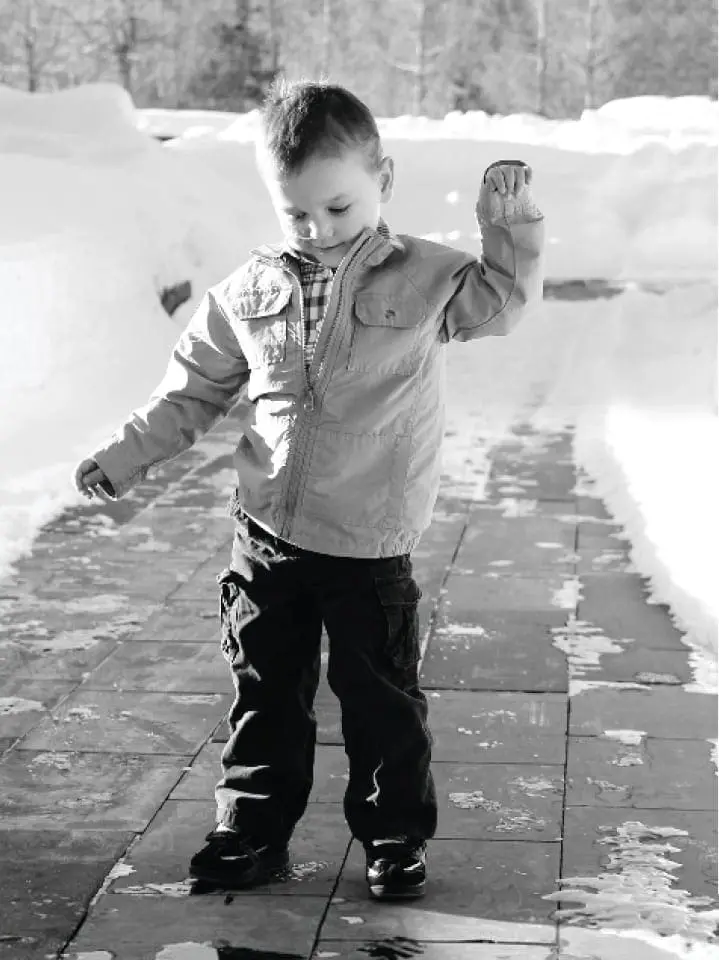 Lukas standing outside in the snow, smiling and holding something in his raised hand.