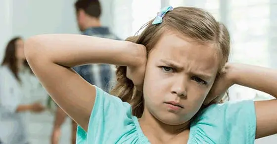 Girl covering her ears with a distressed expression while parents argue in the background.