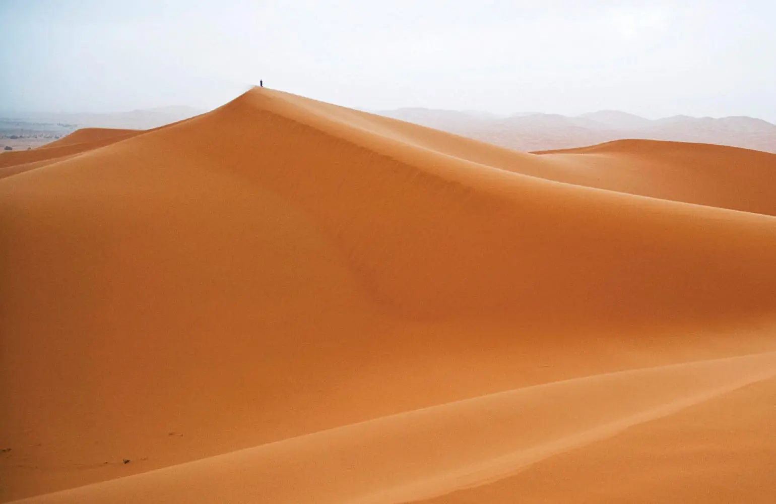 Erg Chebbi, Morocco, with rolling sand dunes under a hazy sky.
