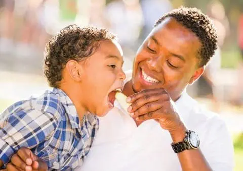 Man feeding a child a piece of food outdoors.