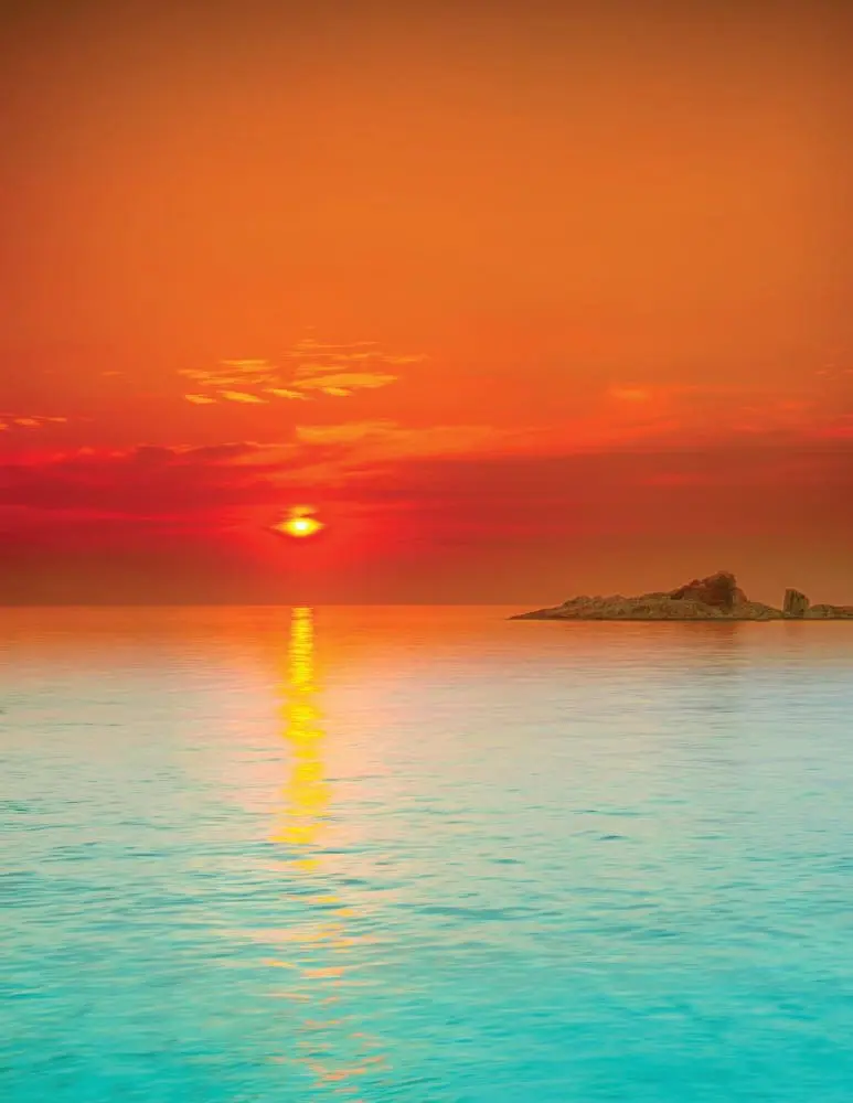 Tropical island silhouette during a vibrant orange and red sunset over the ocean.
