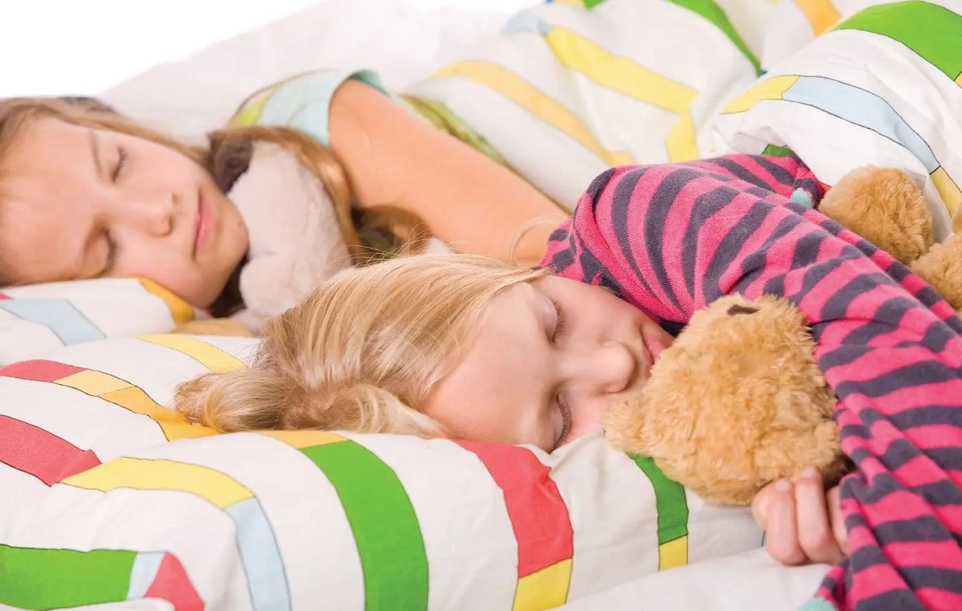Two children sleeping soundly in bed with a teddy bear.
