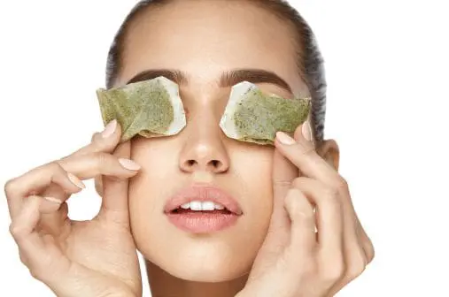 Woman applying used tea bags to her closed eyelids.