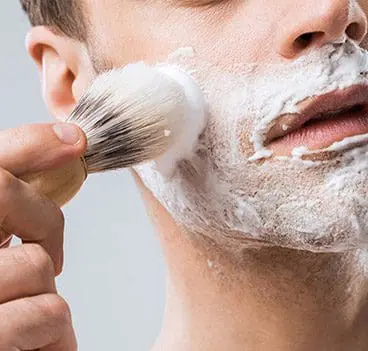 A man applies shaving cream to his face with a brush.