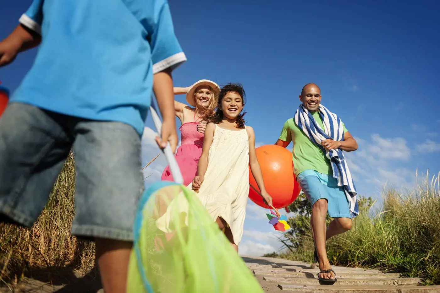 Family walking toward the beach with toys and a beach towel.