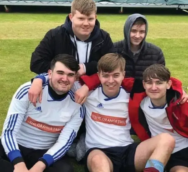 Five young people smile as they sit and pose for a photo outdoors.