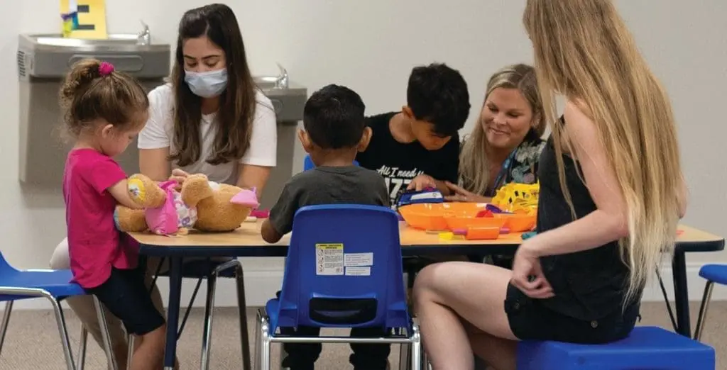 Children and adults interact around a table in an early intervention program.