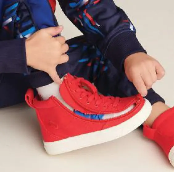 Child's hands putting on a red BILLY Footwear shoe with a zipper closure.