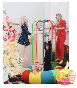 Children playing on a colorful Jungle Jumparoo indoors near a decorated Christmas tree.