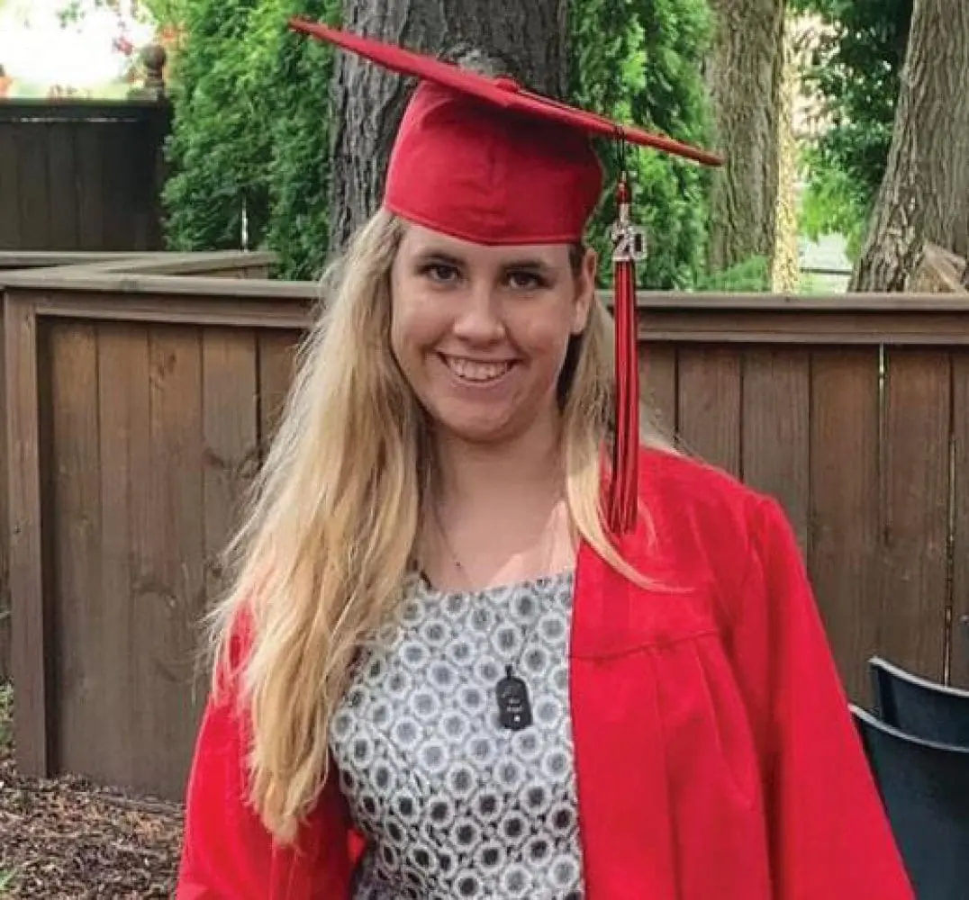 College graduate in a red cap and gown smiling.