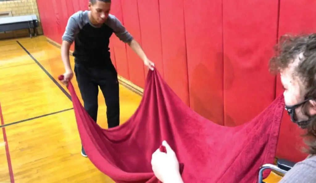 Two people holding a red cloth with bells on it in a gym.