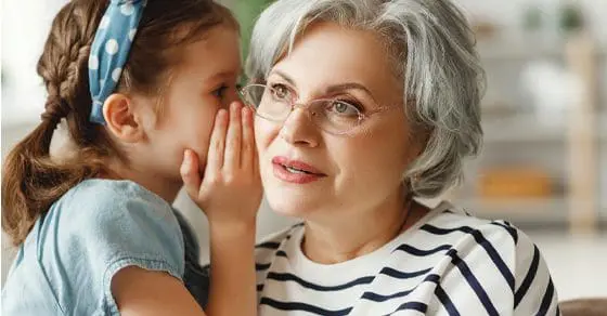 A young girl whispers a secret into an older woman's ear.