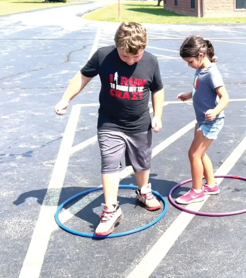 Two children stand inside hula hoops on a paved surface.
