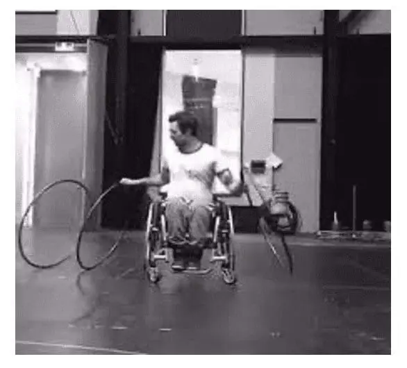 Person in a wheelchair hooping with two hula hoops.