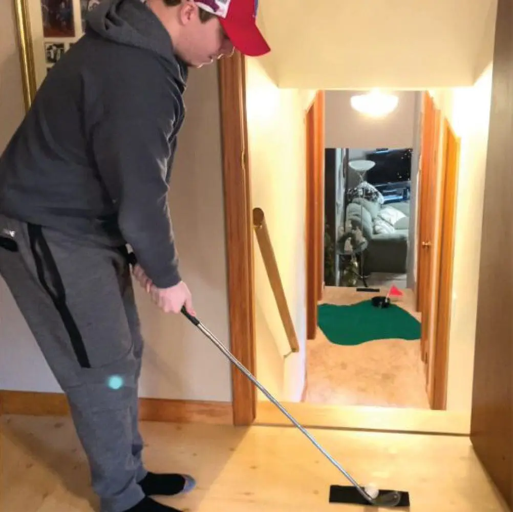Man playing indoor golf in a hallway.