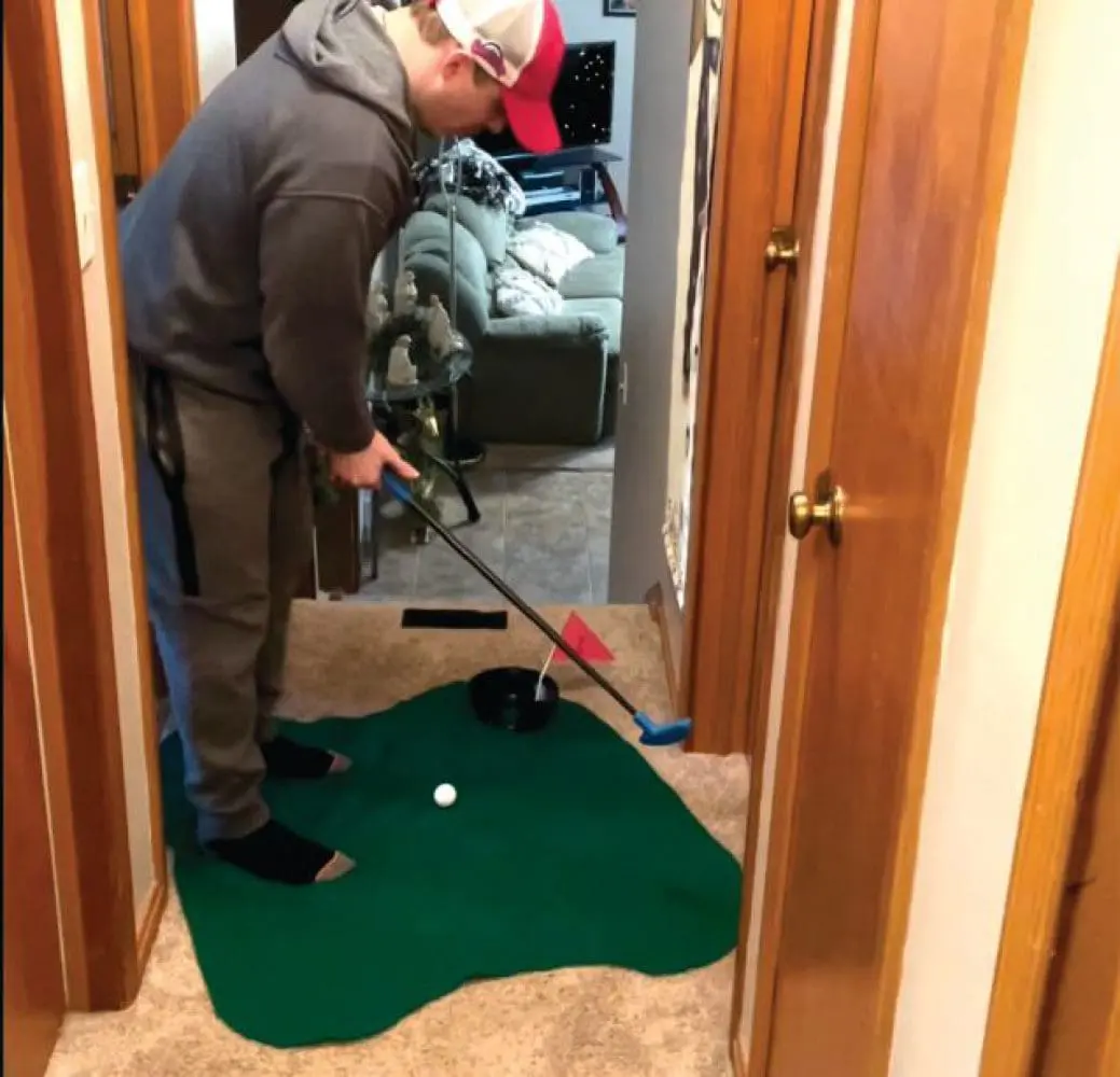 A person practices indoor golf putting on a green mat in a hallway.