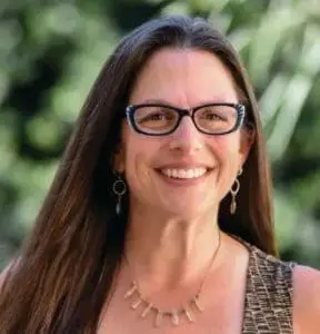 Emily Berman smiling wearing glasses and a necklace.