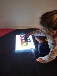 A young child plays with colorful Magformers on a light-up surface.