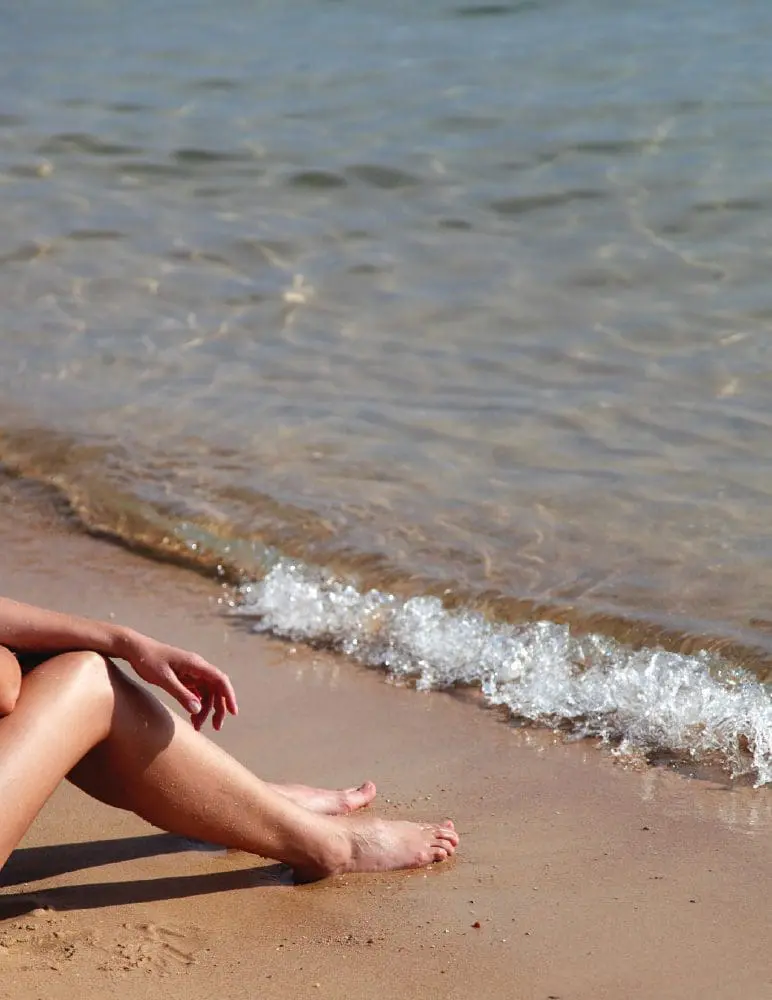 A person sits on a sandy beach with waves lapping at the shore.