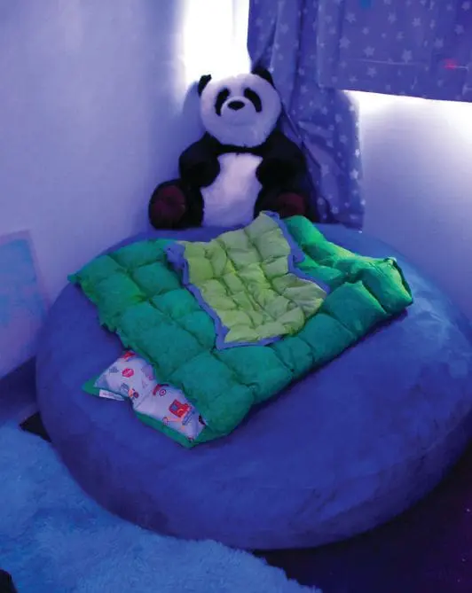 Panda stuffed animal sitting on a blue beanbag with a green blanket.