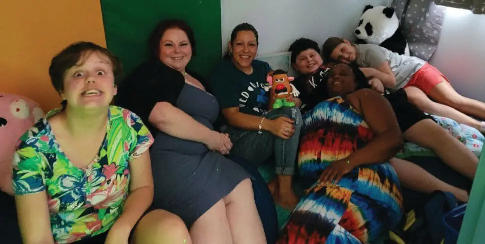 Group of people sitting together in a colorful room with stuffed animals.
