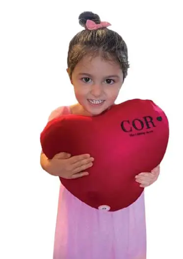 A young girl hugs a red heart-shaped balloon that says "COR".