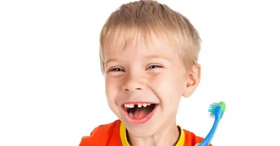 Smiling boy with missing front teeth holds a toothbrush.