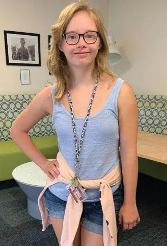 Maggie Scherder wearing a light blue tank top, jean shorts, and glasses.