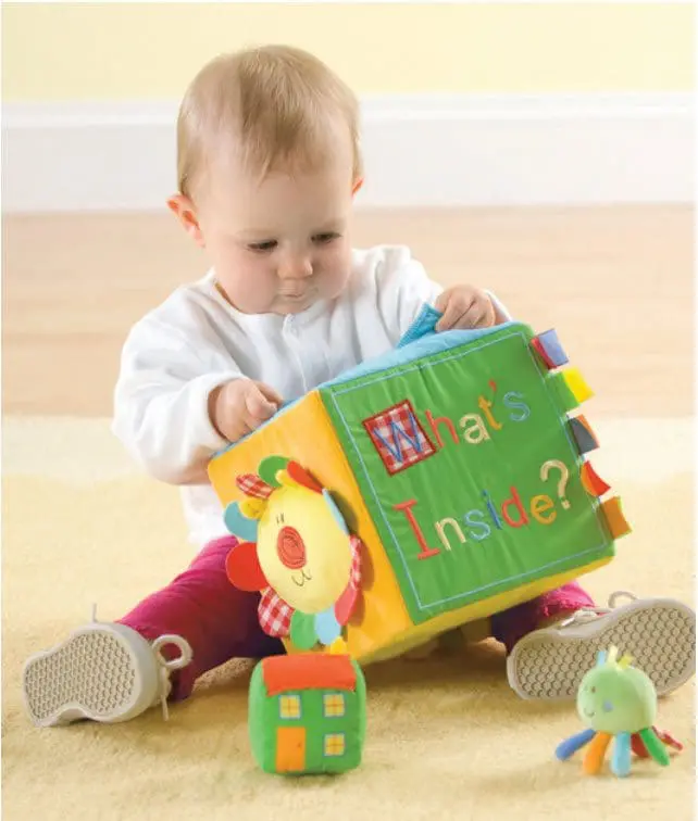 Baby with a soft toy activity cube that says "What's Inside?".