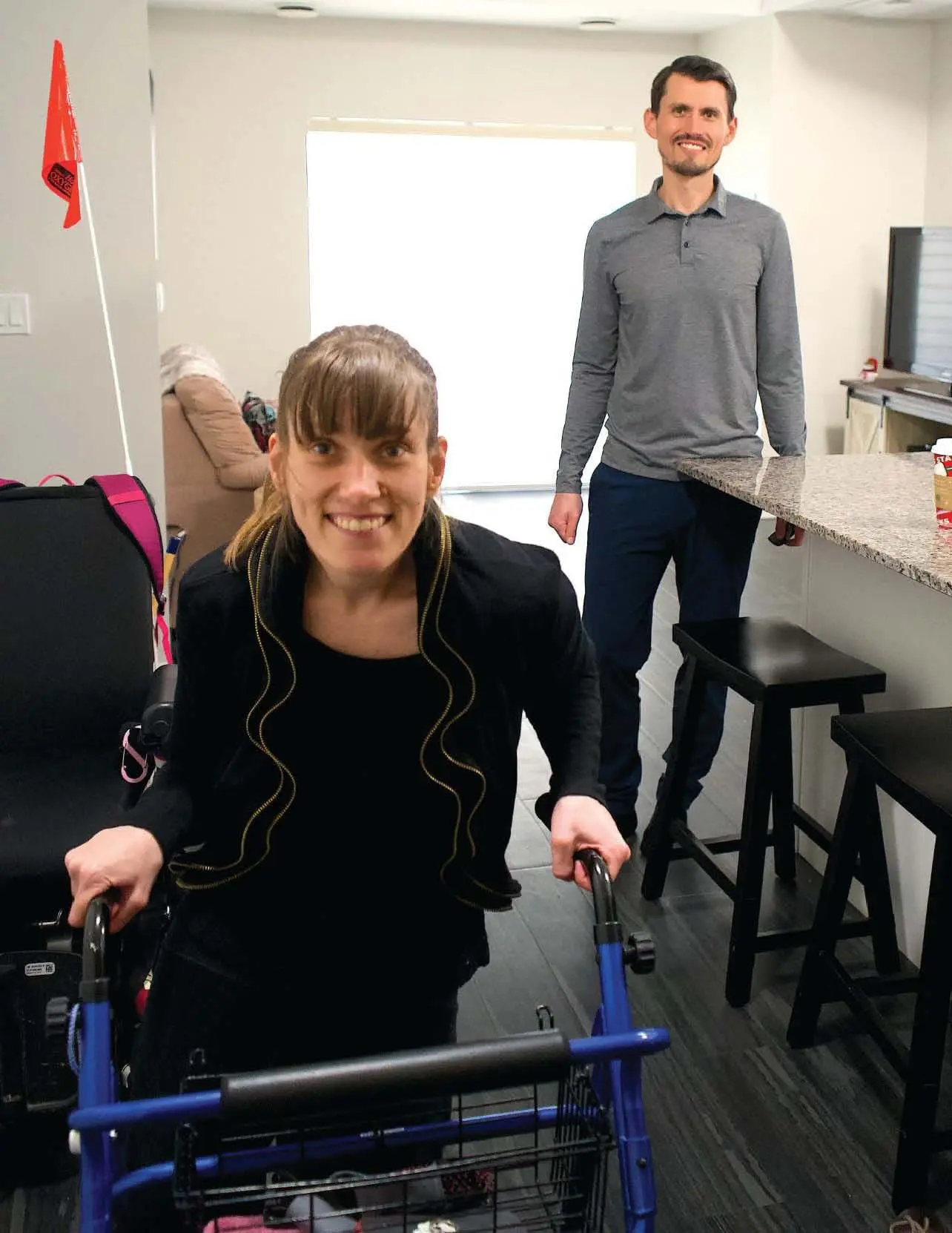 Sarah Goll smiles while holding a walker, with Eric Goll standing behind her.