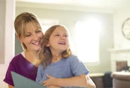 A woman and a child look at a book in a room.