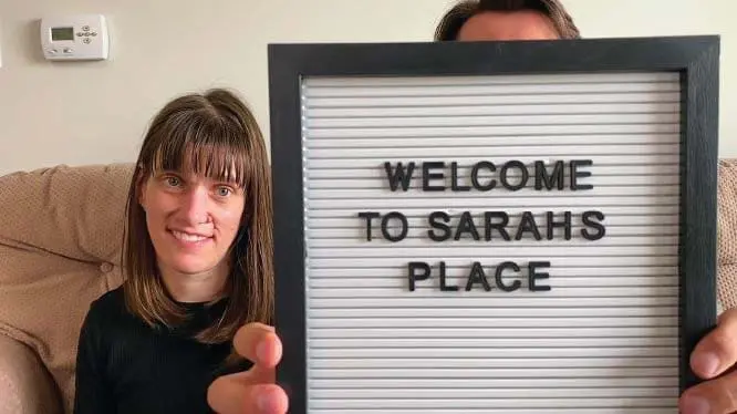 Sarah Goll holding a sign that says "WELCOME TO SARAHS PLACE