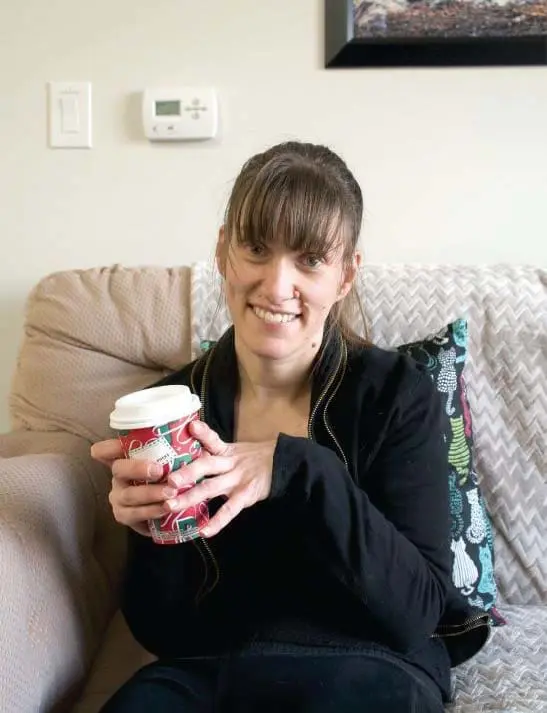 Sarah Goll holding a coffee cup while sitting on a couch.