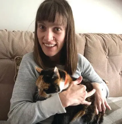 Sarah Goll holding a calico cat while sitting on a couch.