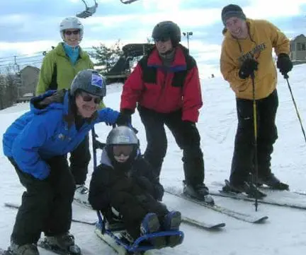 Group of skiers on a snowy slope, one in a specialized sled.