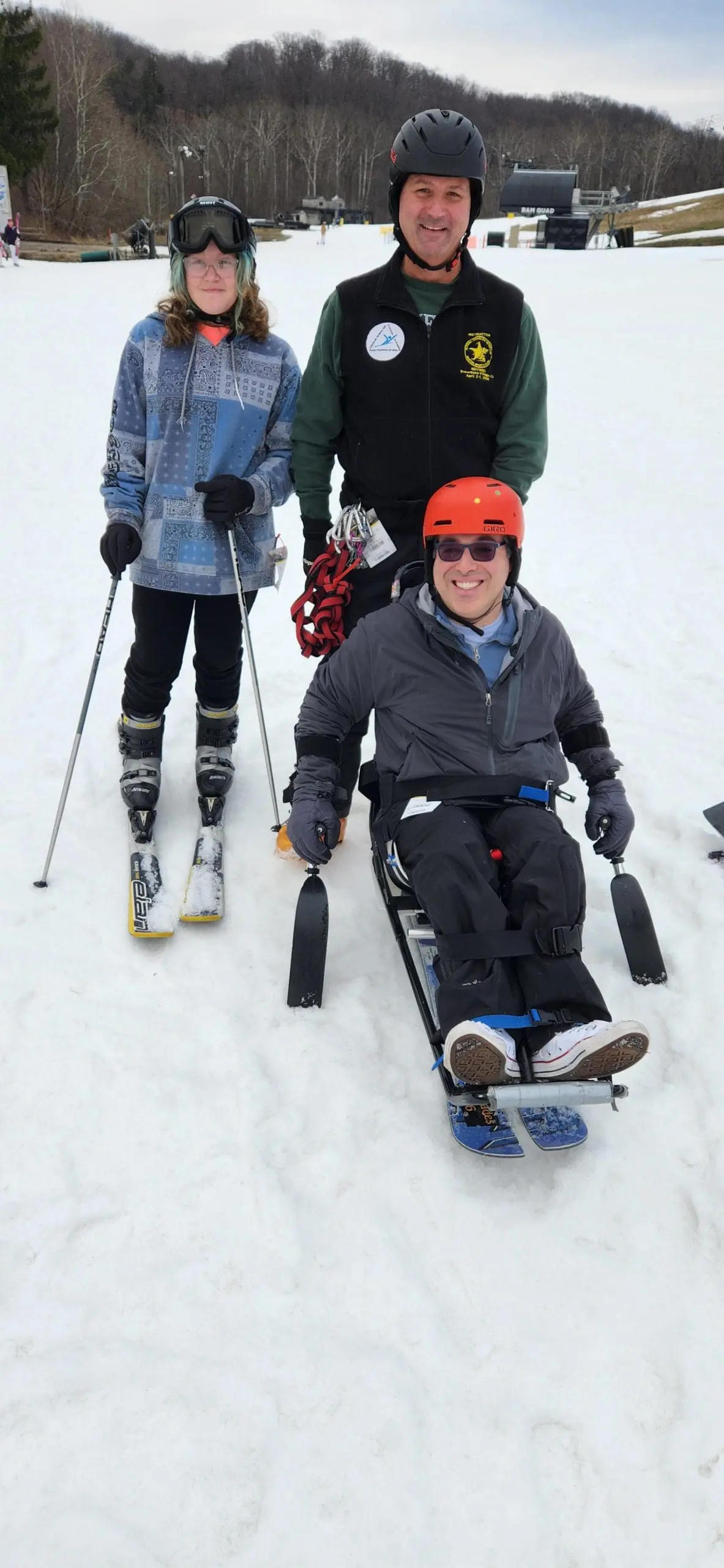 Three people in ski gear on a snowy slope, one in a sit-ski.