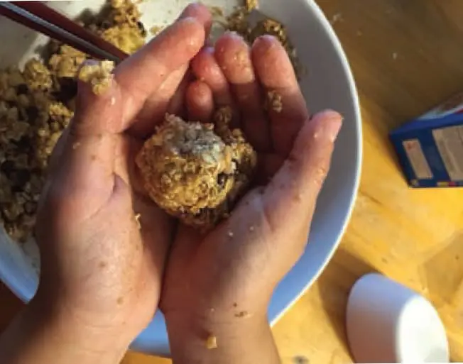 Hands rolling granola mixture into a ball over a mixing bowl.