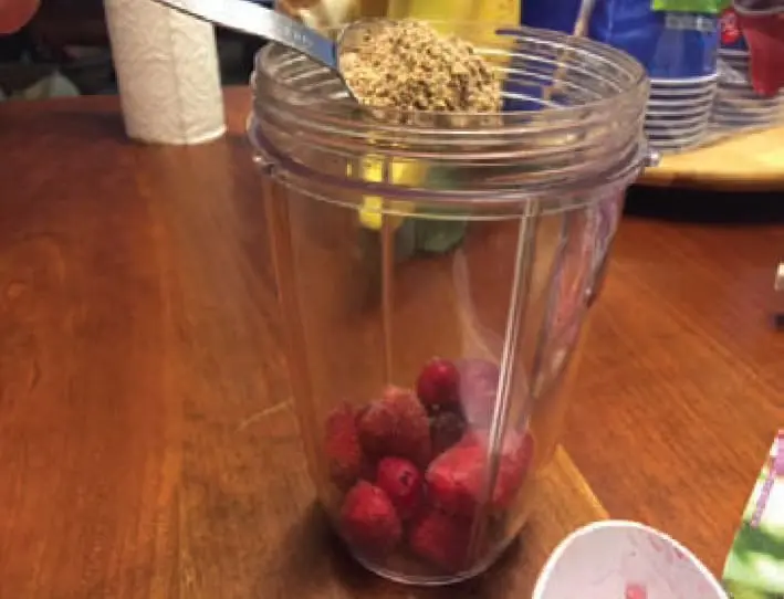Spoonful of seeds being added to blender with frozen berries.