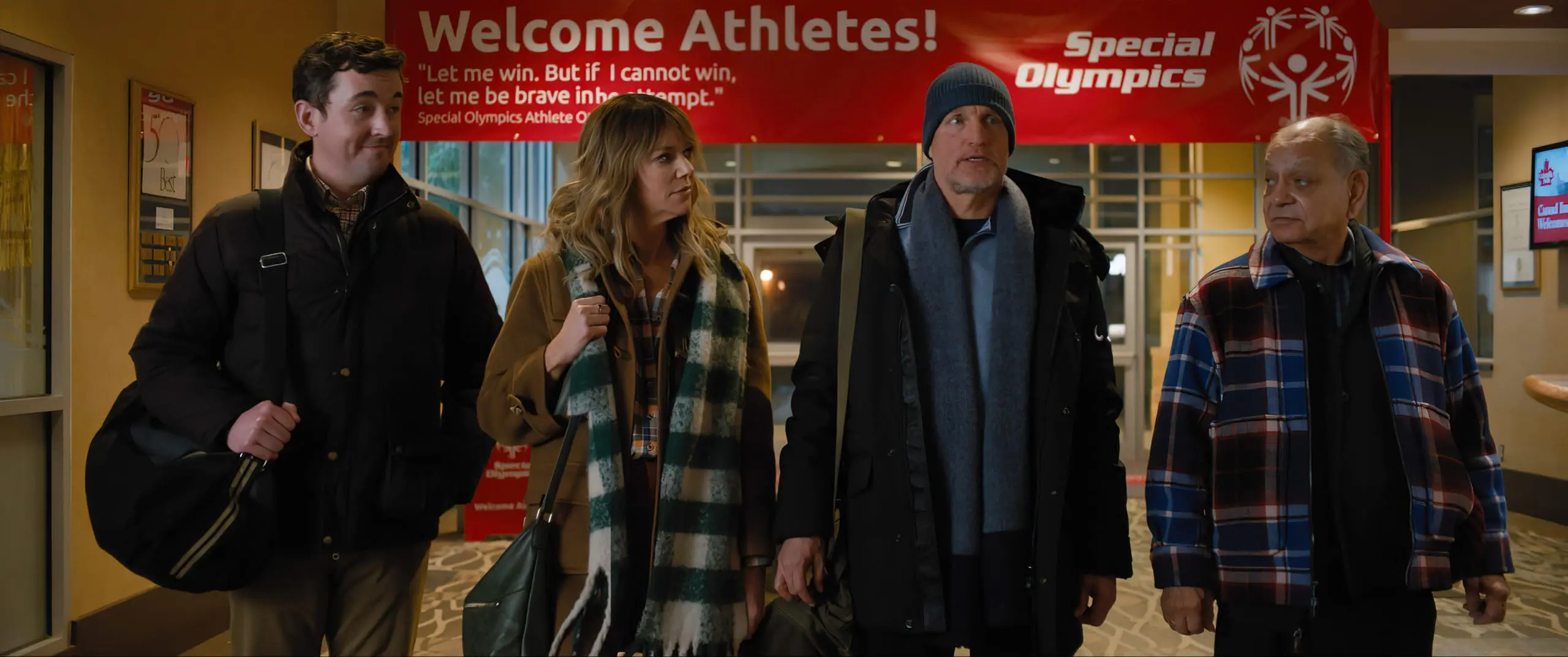 Four people walk past a banner that reads "Welcome Athletes! Special Olympics.