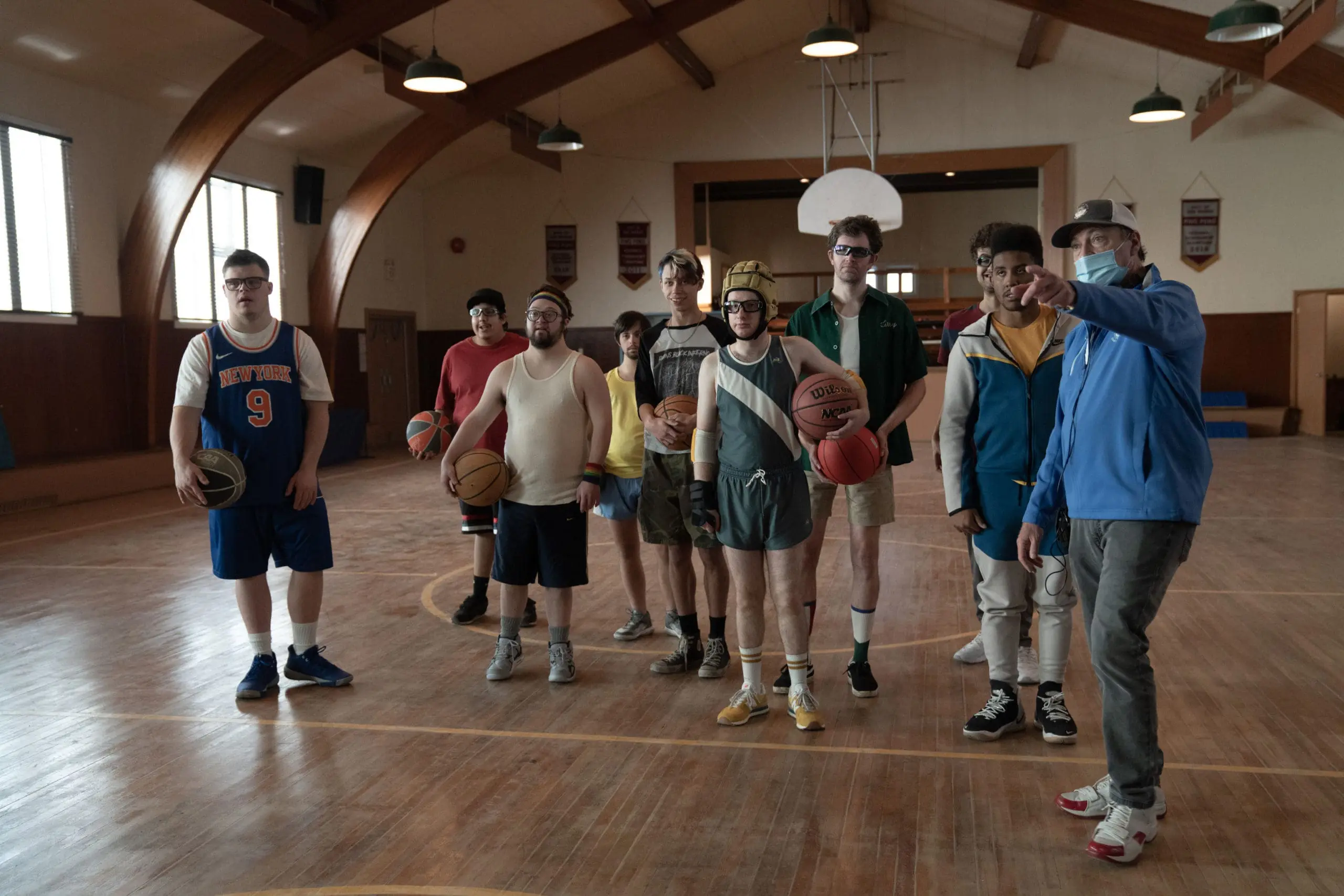 A group of ten men and boys stand on a basketball court, most holding basketballs.
