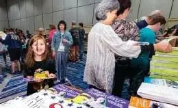 Children and adults browsing a table of books and materials at an event.