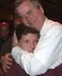 Two men embracing, one with closed eyes.