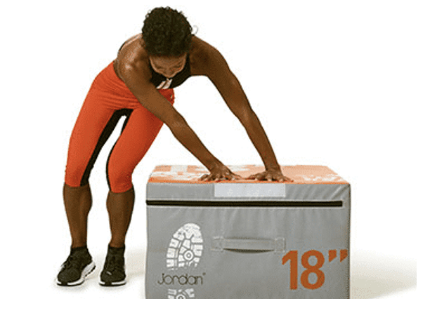 A woman in athletic wear places her hands on a gray exercise box labeled "18".