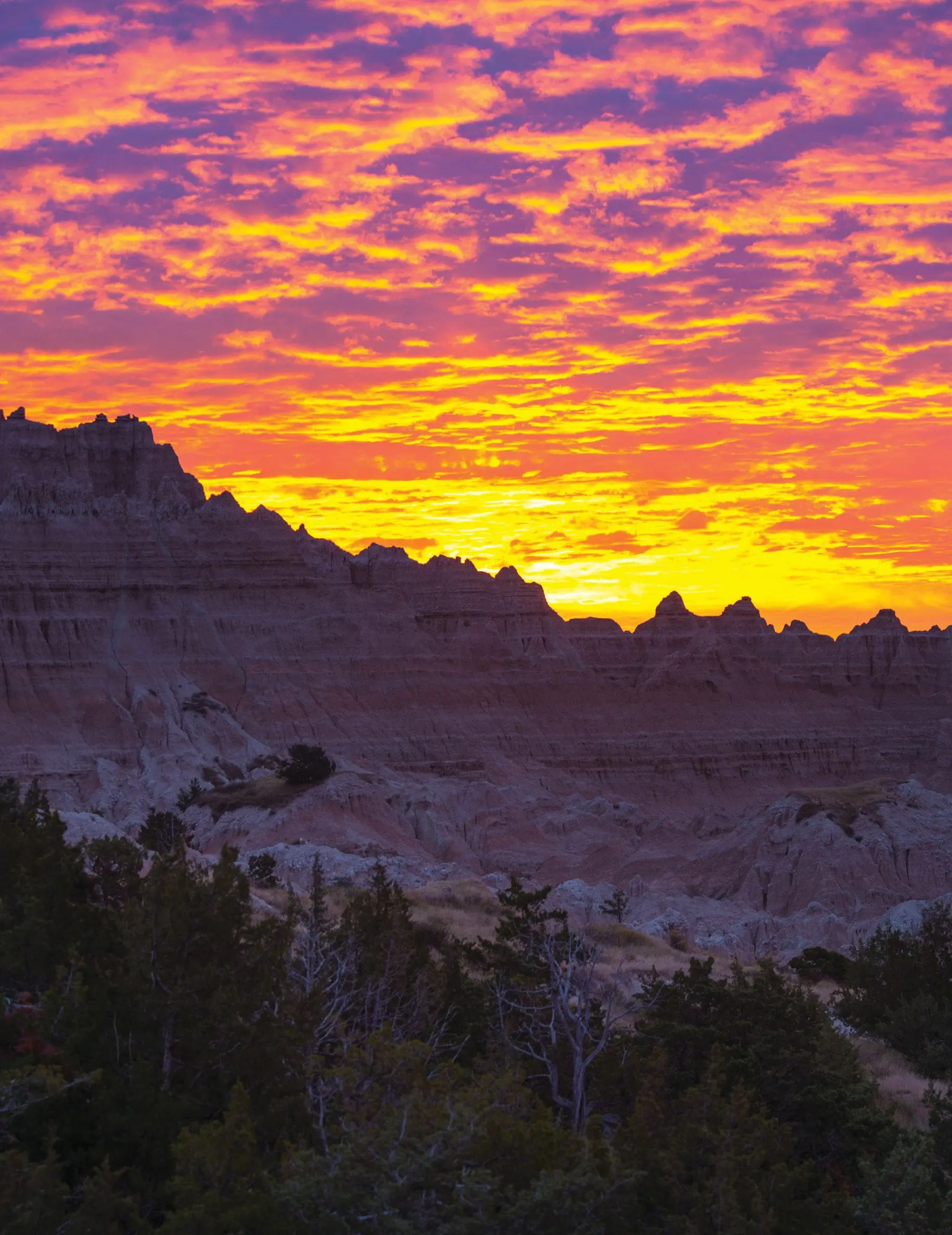Pink and orange sunrise casting a warm glow over the rugged rock formations of Badlands National Park.