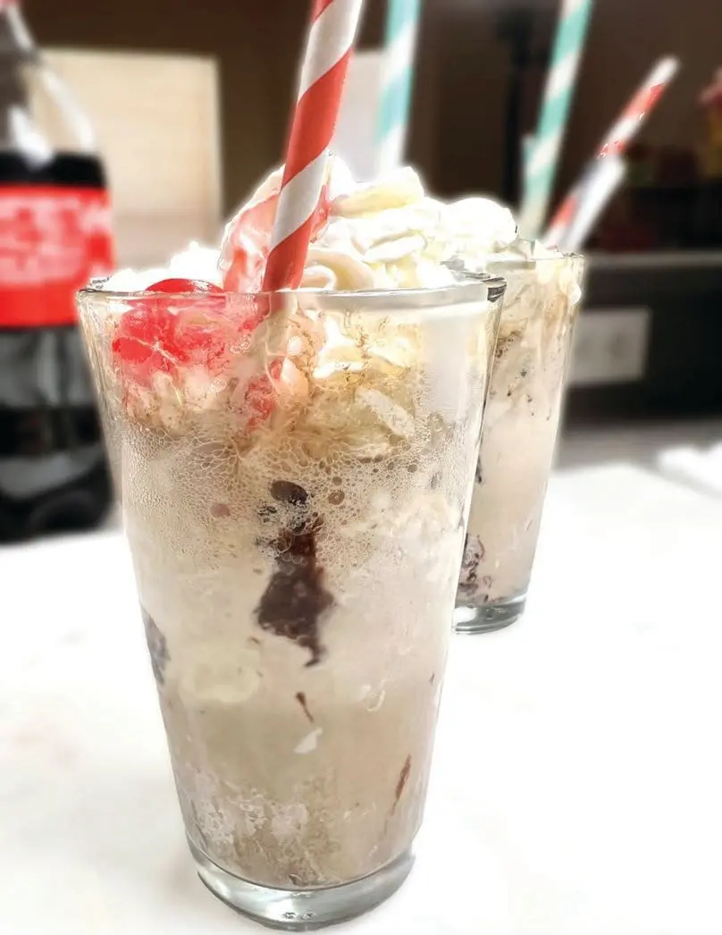 Two old-fashioned ice cream sodas with whipped cream and cherries.