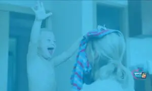 A child with arms raised in excitement is facing away from a woman holding clothing.