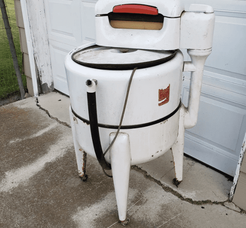 White vintage wringer washing machine with a red logo and black hoses.