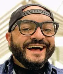 Derek Flores smiling broadly while wearing glasses and a baseball cap.