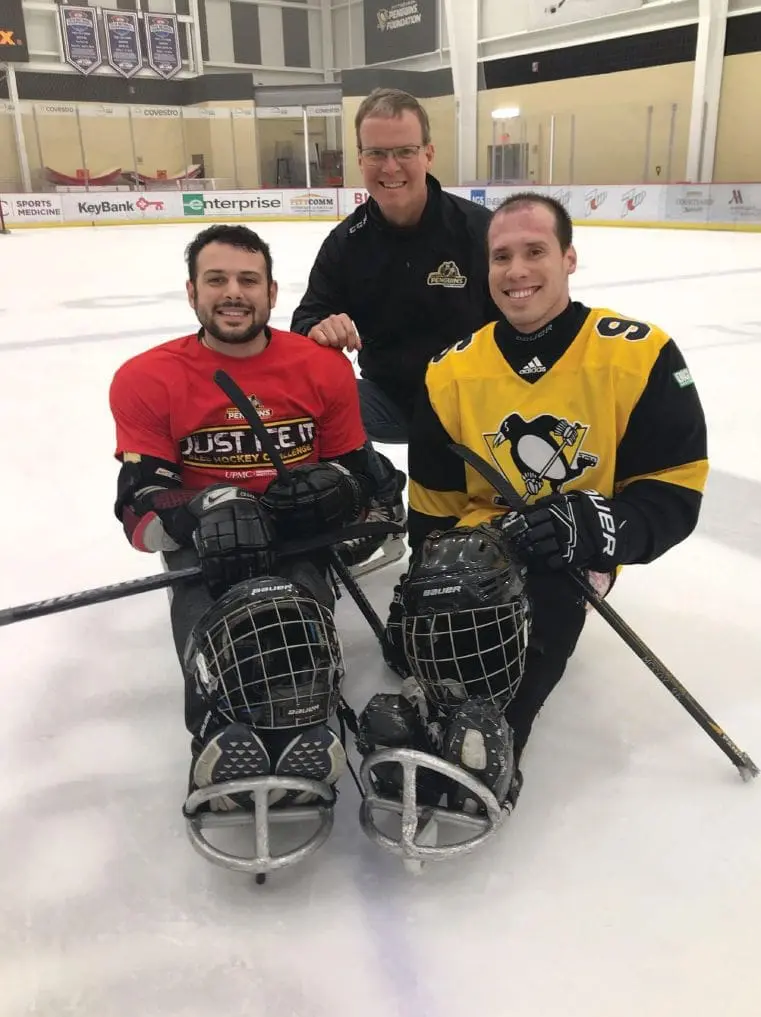 Dr. Andrew McCoy and two other men in hockey gear on an ice rink.