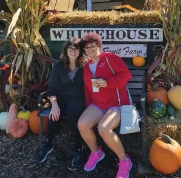 Dr Emily Gianetti and her sister sit on a bench in front of a sign that says White House Fruit Farm.